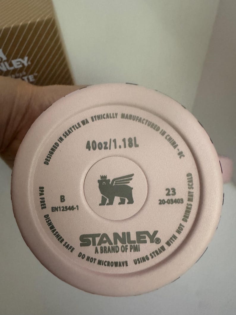 May include: A pink Stanley brand tumbler bottom with the text "40oz/1.18L". The tumbler is dishwasher safe and BPA free. The bottom also features the Stanley logo and a winged bear logo.