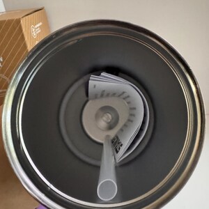 May include: A stainless steel tumbler with a gray interior, a clear straw, and a lid with a central opening. The lid has a small, circular opening for the straw. A folded paper with text is inside the tumbler.
