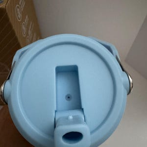 Puede incluir: Tapa de botella de agua azul claro con una abertura abatible y un peque&ntilde;o respiradero. La tapa tiene un dise&ntilde;o circular con un asa a cada lado. La tapa es de pl&aacute;stico y tiene un acabado mate.