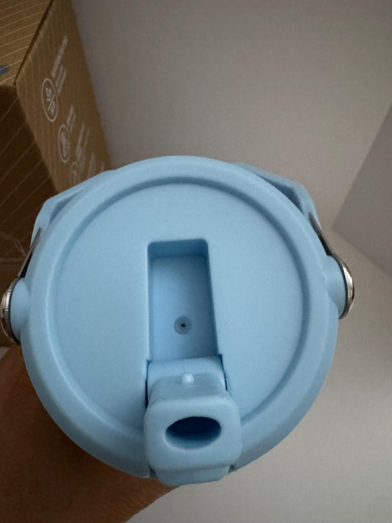 Puede incluir: Tapa de botella de agua azul claro con una abertura abatible y un peque&ntilde;o respiradero. La tapa tiene un dise&ntilde;o circular con un asa a cada lado. La tapa es de pl&aacute;stico y tiene un acabado mate.