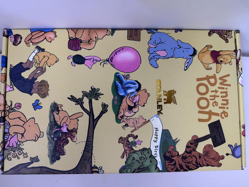 K&ouml;nnte beinhalten: Eine rechteckige Box mit gelbem Hintergrund mit Illustrationen von Winnie-the-Pooh-Charakteren. Die Box hat die Worte "Winnie the Pooh" in brauner Schrift. Die Box hat auch das Stanley-Logo.