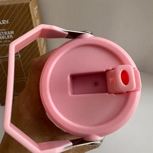 May include: A pink Flow Straw Tumbler lid with a handle. The lid has a flip-top opening and a handle for easy carrying. The tumbler is designed for cold beverages. The lid is made of plastic and has a smooth finish.