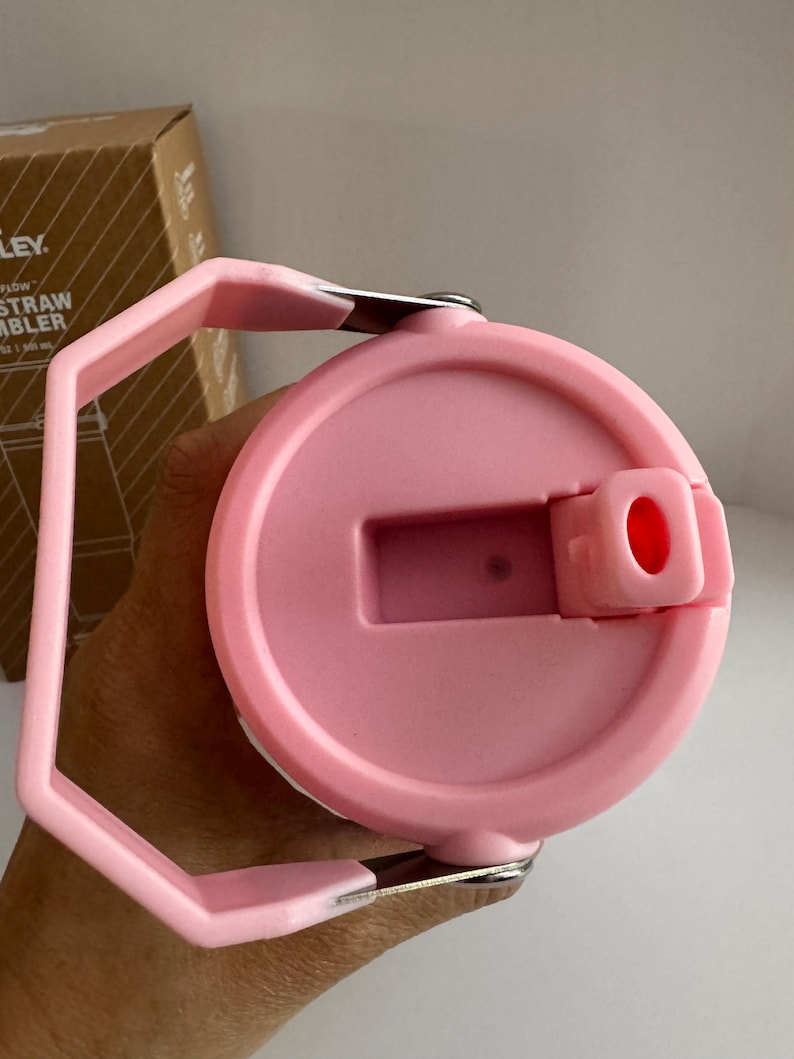 May include: A pink Flow Straw Tumbler lid with a handle. The lid has a flip-top opening and a handle for easy carrying. The tumbler is designed for cold beverages. The lid is made of plastic and has a smooth finish.