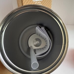 May include: A stainless steel Stanley Flip Straw Tumbler, 30 oz capacity, with a gray straw and interior. The tumbler's interior is visible, along with the straw and a folded product information tag. The top of the tumbler is open, revealing the inside.