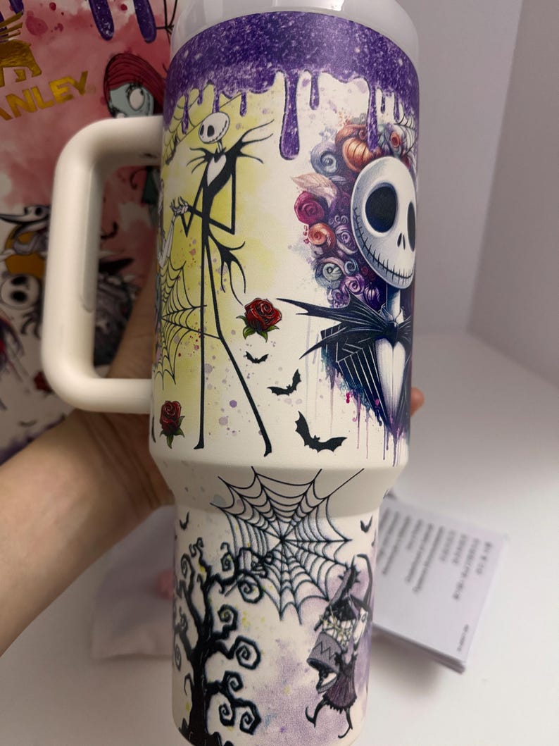 Puede incluir: Un vaso aislado blanco con un dise&ntilde;o colorido de Jack Skellington de The Nightmare Before Christmas. El dise&ntilde;o incluye murci&eacute;lagos, rosas y una telara&ntilde;a. La parte superior tiene un dise&ntilde;o de goteo p&uacute;rpura y un asa blanca.