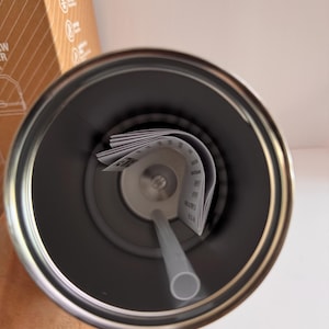 May include: A stainless steel tumbler with a gray straw and a paper insert. The interior of the tumbler is dark gray, and the straw is light gray. The tumbler is designed to keep drinks cold or hot.