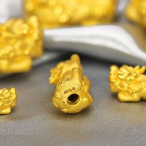 May include: A close-up of a gold-colored Chinese dragon charm. The charm is detailed and intricate, with a small hole in the center for threading.