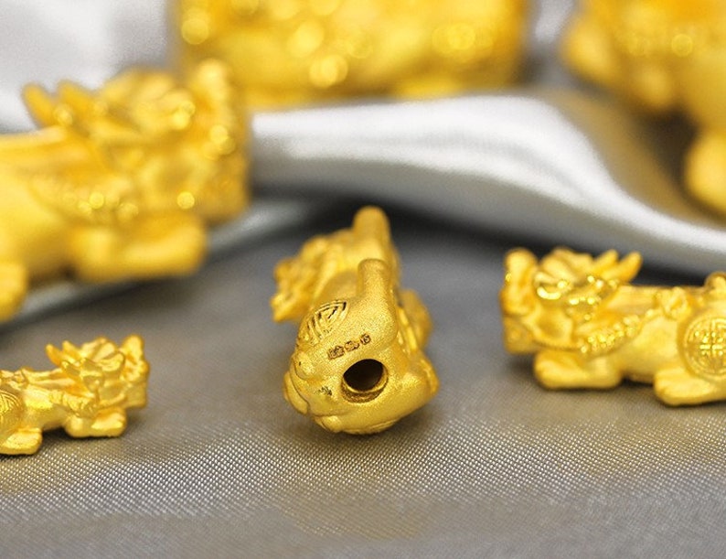 May include: A close-up of a gold-colored Chinese dragon charm. The charm is detailed and intricate, with a small hole in the center for threading.