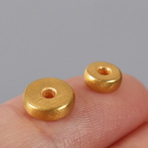 May include: Two gold-colored metal beads with a hole in the center. The beads are round and have a smooth, slightly textured surface.
