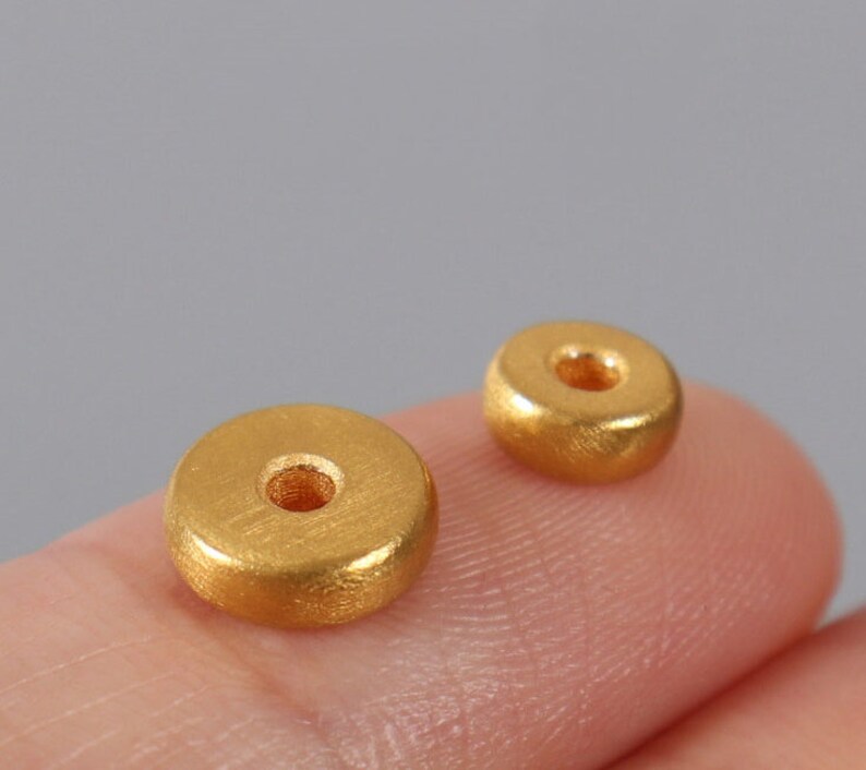 May include: Two gold-colored metal beads with a hole in the center. The beads are round and have a smooth, slightly textured surface.