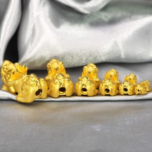 May include: A set of seven gold-colored lion charms of varying sizes. The charms are detailed with intricate designs and are arranged in a row on a silver fabric background.