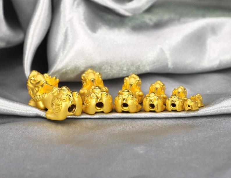 May include: A set of seven gold-colored lion charms of varying sizes. The charms are detailed with intricate designs and are arranged in a row on a silver fabric background.