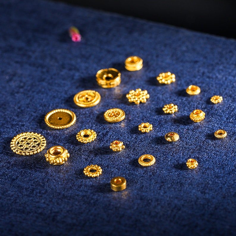 May include: A collection of gold-colored metal beads with various designs and sizes. The beads are arranged on a blue surface.