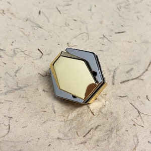 May include: A gold hexagonal shaped object with a silver frame. The object is made of metal and has a shiny finish.