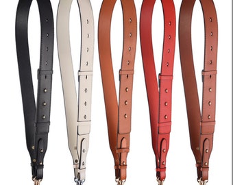 May include: Five leather camera straps in different colors: black, beige, brown, red, and brown. Each strap has a metal buckle and a metal loop.