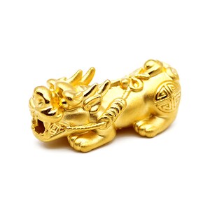 May include: A gold-colored pendant in the shape of a mythical creature, possibly a lion or dragon, with intricate details and a rope-like design around its neck.