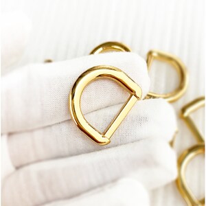 以下が含まれることがあります： 金色の金属製のDリング。ストラップ、チェーン、その他のアクセサリーを取り付けるための金具の一種です。