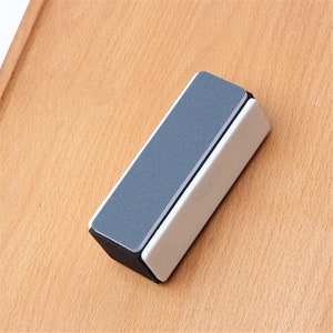 May include: A black and white nail file with two sides. One side is a coarse grit and the other side is a fine grit.