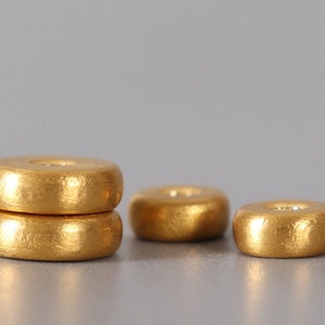 May include: Three gold-colored wooden beads, stacked on top of each other. The top bead is slightly larger than the bottom two beads.