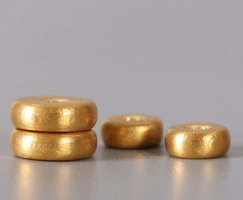 May include: Three gold-colored wooden beads, stacked on top of each other. The top bead is slightly larger than the bottom two beads.