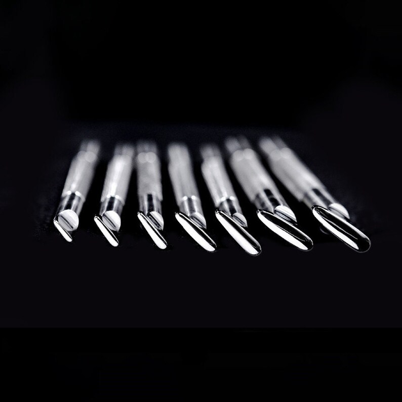 Pu&ograve; includere: Un set di dieci strumenti in metallo argentato con punte di diverse forme, disposti in fila su una superficie nera.