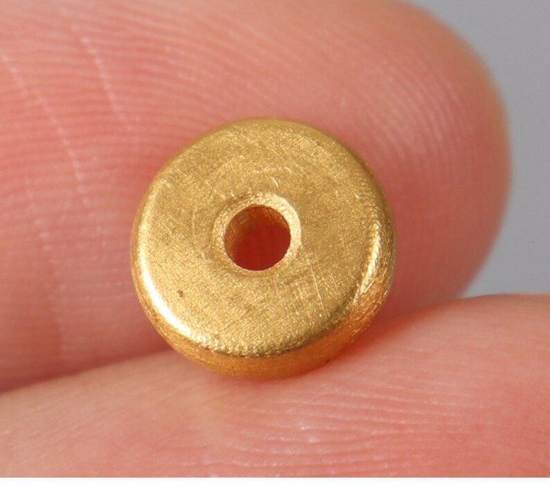 May include: A gold-colored metal bead with a round hole in the center. The bead has a smooth, slightly textured surface.
