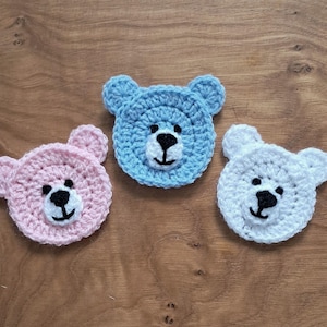 May include: Three crocheted teddy bear appliques in pink, blue and white. The bears have black eyes and noses.