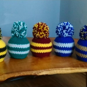 May include: Five crocheted hats with pom-poms in different colour combinations. The hats are striped with yellow, black, green, white, maroon, blue, and brown.