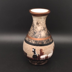 May include: A ceramic vase with a narrow neck and a rounded body, featuring a cream-colored base with black horsehair-style markings. A horizontal copper band encircles the middle, and a painted scene depicts a black figure and white animals.