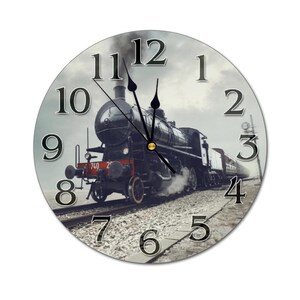 May include: Round wall clock featuring a vintage black steam train on a track, set against a cloudy sky. The clock face has large black numerals and hands, with the time displayed at approximately 11:00. The clock is a decorative item.