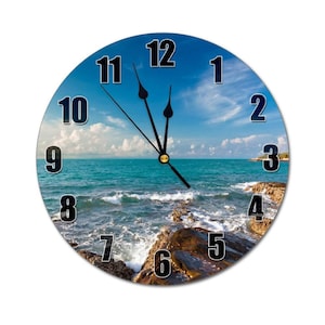 May include: A round clock with a blue sky and ocean scene. The clock face has black numbers and hands. The ocean scene features waves crashing on rocks.