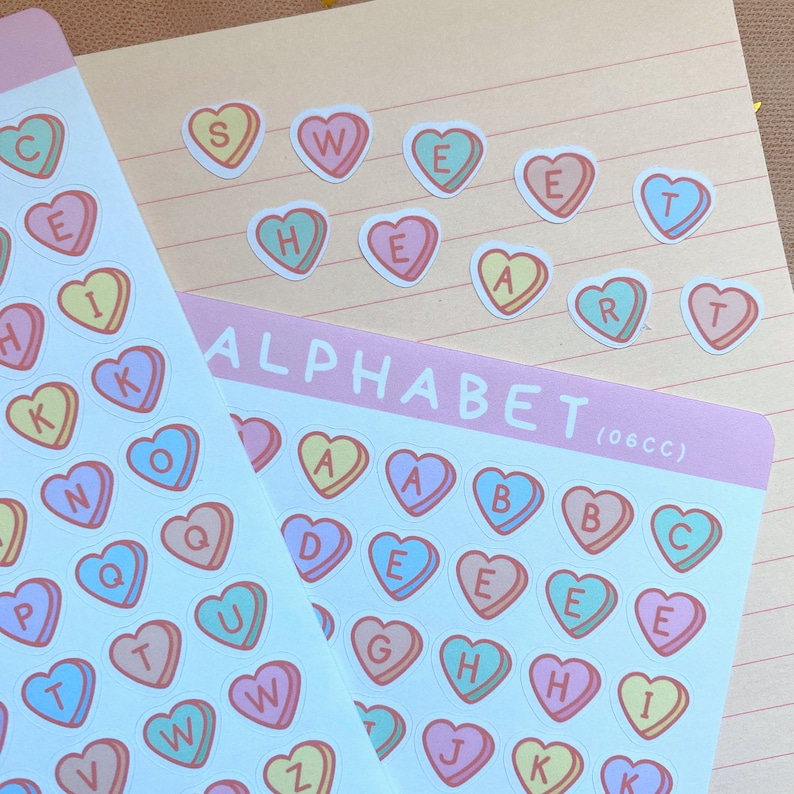 May include: Two sheets of stickers with alphabet letters in the shape of candy hearts. The top sheet has the word "SWEET HEART" spelled out in candy hearts. The bottom sheet has the alphabet in candy hearts, with the title "ALPHABET (06CC)".
