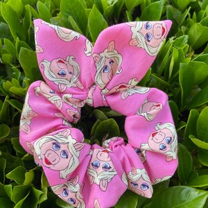 Peut inclure: Un chouchou rose avec un motif r&eacute;p&eacute;t&eacute; du visage de Miss Piggy.