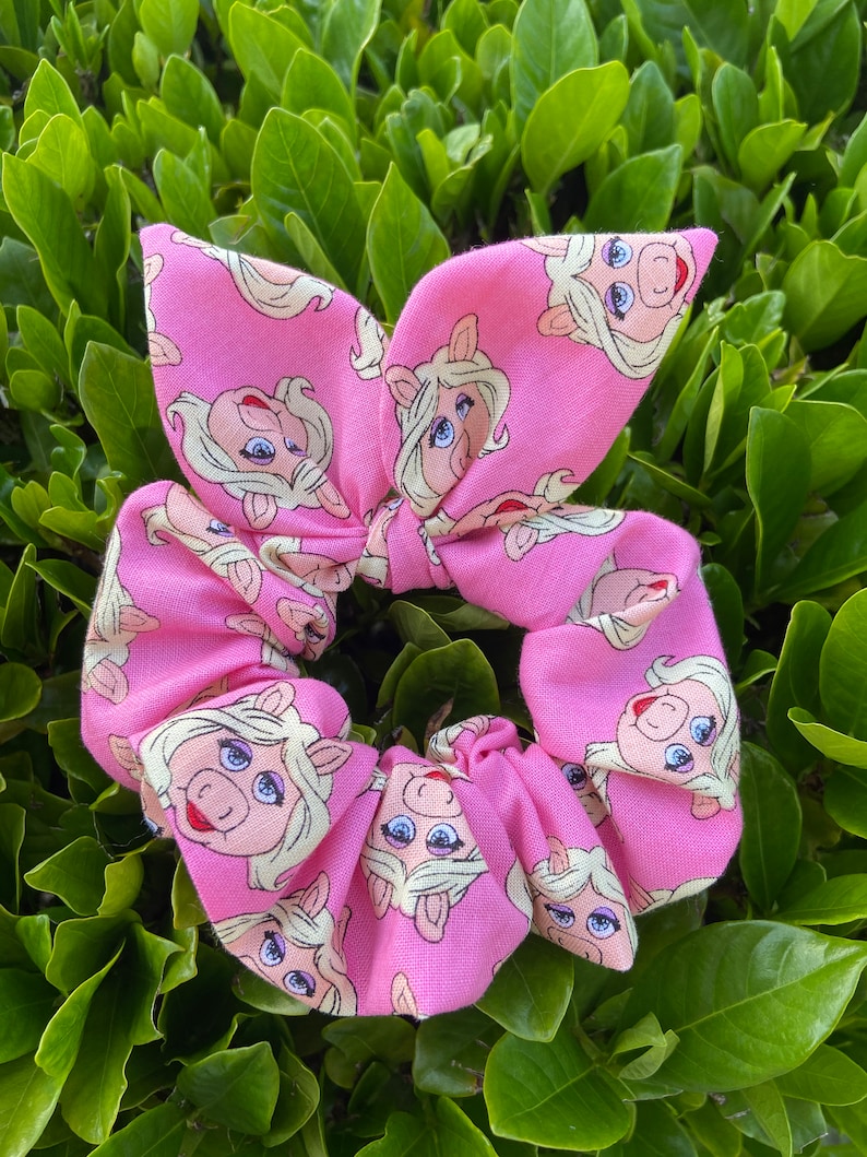 Peut inclure: Un chouchou rose avec un motif r&eacute;p&eacute;t&eacute; du visage de Miss Piggy.