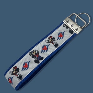 May include: A white and blue key chain with a repeating pattern of Mickey Mouse and Minnie Mouse holding hands with a red heart and a blue wave design. The key chain has a silver metal ring.