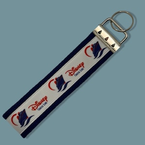 May include: A blue and white key chain with the Disney Cruise Line logo and a ship design. The key chain has a silver metal ring.