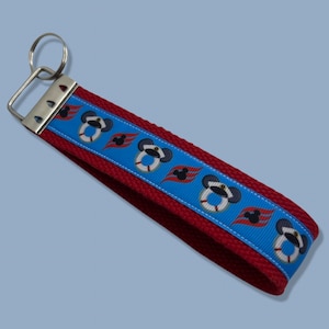 May include: Red and blue key chain with a Mickey Mouse design. The key chain features a repeating pattern of Mickey Mouse wearing a captain's hat and a life preserver, along with the Disney Cruise Line logo.