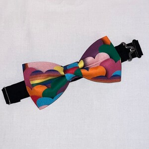 May include: A colorful bow tie with a pattern of overlapping circles and a rainbow stripe. The bow tie is attached to a black elastic band.