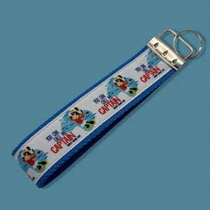 May include: Blue and white key chain with a repeating pattern of Mickey Mouse in a boat with the text "You can call me Captain".