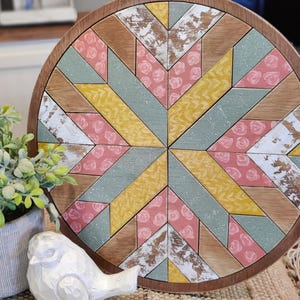 May include: A round wooden tray with a geometric pattern in shades of pink, yellow, and green. The tray has a distressed, rustic look and is perfect for serving snacks or drinks.