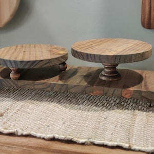 May include: A wooden tiered stand with two round platforms and four legs. The stand is made of natural wood with a dark brown finish and a rustic look.