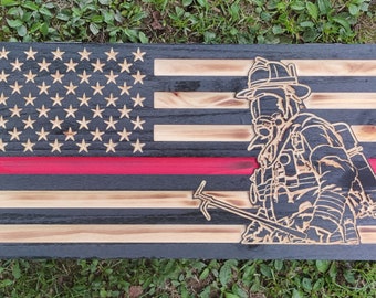 May include: A wooden American flag with a red stripe across the middle and a firefighter silhouette in the right half of the flag. The flag is made of reclaimed wood and has a distressed look.