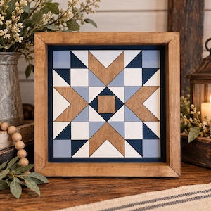 May include: A square wooden wall art piece featuring a geometric quilt block pattern. The design consists of a central square surrounded by triangles and squares in shades of navy blue, light blue, white, and natural wood grain, all encased in a frame.