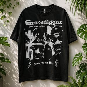 May include: A black short-sleeved t-shirt featuring a white graphic print of the hip-hop group Gravediggaz. The design includes the text Gravediggaz, Nowhere to Run, and Nowhere to Hide, alongside stylised portraits of the group members.