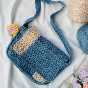May include: A blue crocheted shoulder bag with a colourful crocheted strap and a rainbow-coloured crocheted charm. The bag has a light blue and pink patterned design.
