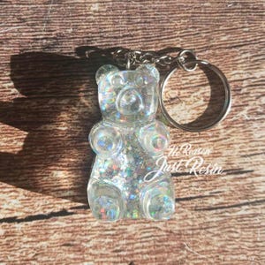 May include: A clear gummy bear keychain filled with iridescent glitter. The keychain has a silver keyring and chain. The text "No Reason Just Resin" is visible on the bottom right of the bear.