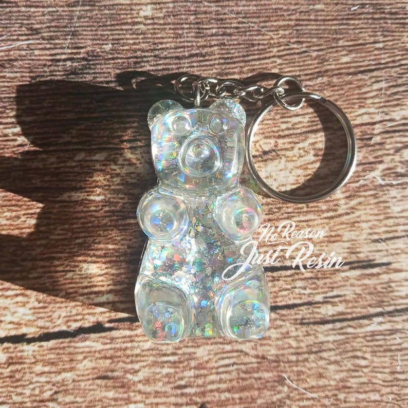 May include: A clear gummy bear keychain filled with iridescent glitter. The keychain has a silver keyring and chain. The text "No Reason Just Resin" is visible on the bottom right of the bear.