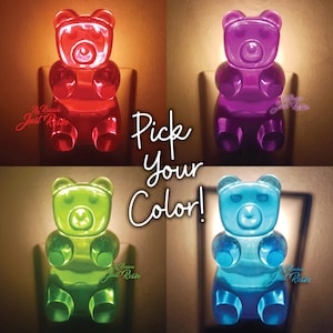 May include: A set of four translucent gummy bear-shaped night lights in red, purple, green, and blue, each plugged into a wall outlet. The text Pick Your Color is centered in white script over the four illuminated bear figures.