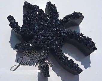 Puede incluir: Escultura de resina negra con forma de araña, con una superficie texturizada similar a un cristal. La araña tiene ocho patas y un cuerpo cubierto de pequeños cristales oscuros y brillantes. El texto "No Reason Just Resin" está escrito en la parte inferior.