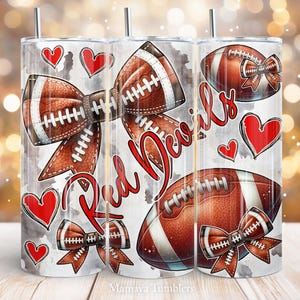 May include: White tumbler with a red, white, and brown football design. The tumbler has a bow made of a football and the words "Red Devils" in red lettering.